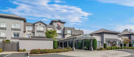 A modern hotel with a covered entrance, a wheelchair-accessible parking space, and a clear blue sky.