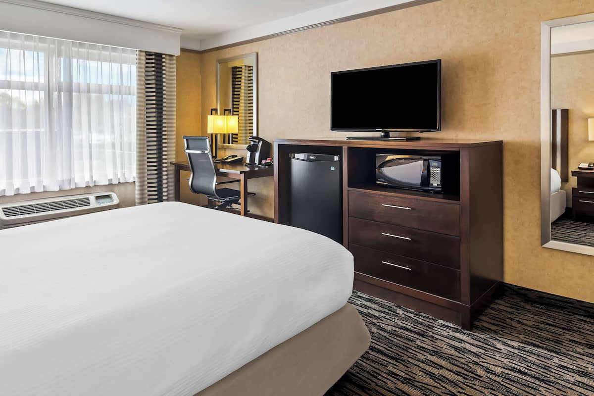 A hotel room with a bed, a desk with a computer, a microwave, a refrigerator, and a television.
