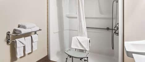 Un baño con ducha, un perchero con toallas dobladas y un taburete.