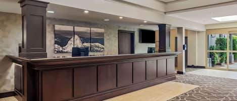 A reception desk with a large window, a flat-screen TV, and a wall-mounted artwork of a mountain scene.