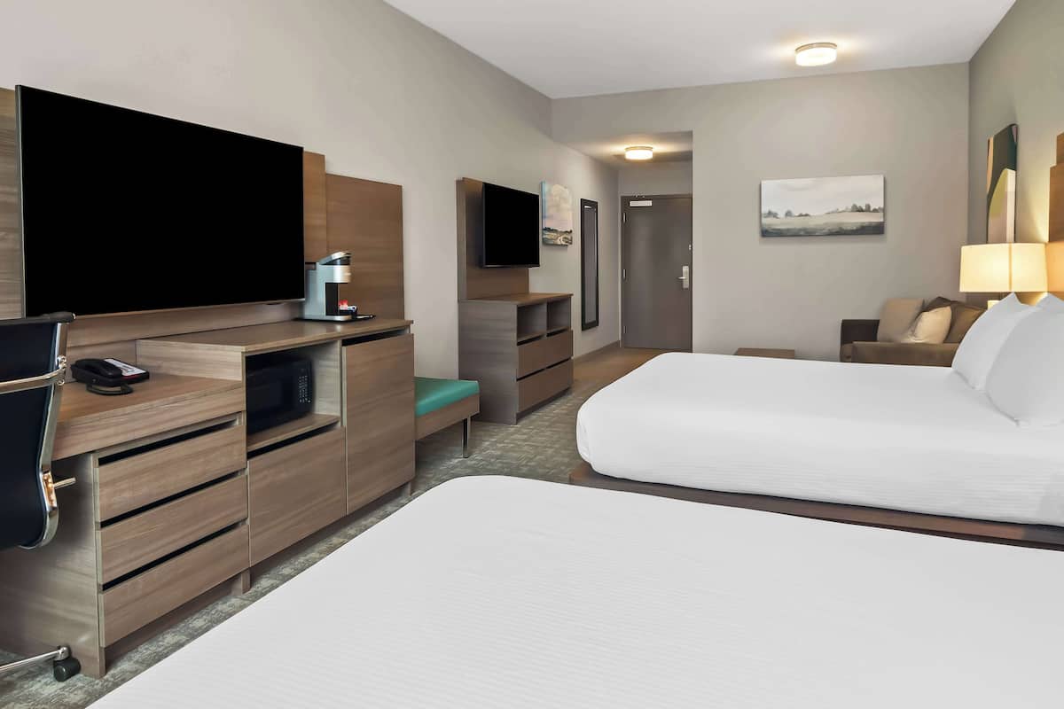 A hotel room with two beds, a TV, a desk with a phone, a microwave, and a coffee maker.
