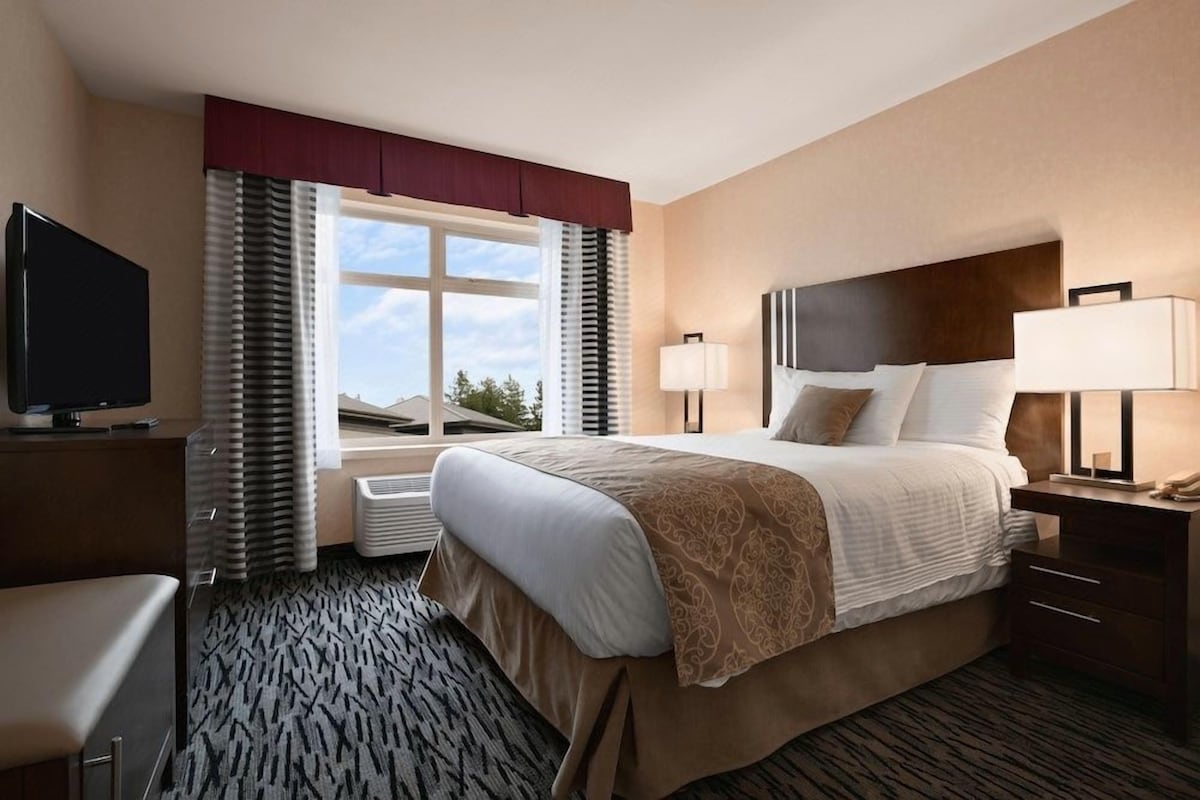 A hotel room with a bed, bedside lamps, a TV, a desk, and a window with curtains.