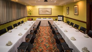 A conference room with long tables set for a meeting, chairs arranged in rows, a projector, and framed artwork on the walls.