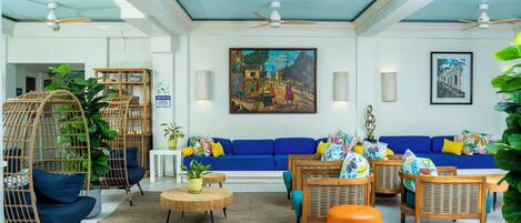 Un salon spacieux avec un canapé bleu, des fauteuils en osier, une table basse et un ventilateur de plafond.