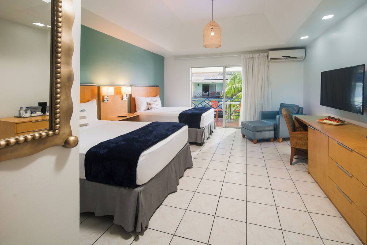 A hotel room with two beds, a TV, a desk, and a balcony with a view.