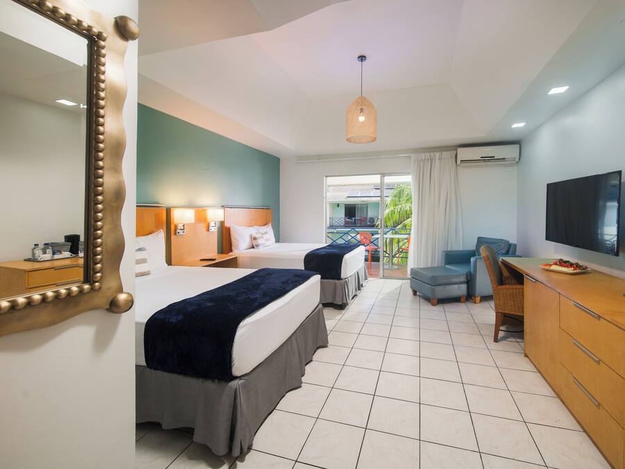 A hotel room with two beds, a TV, a desk, and a balcony with a view.