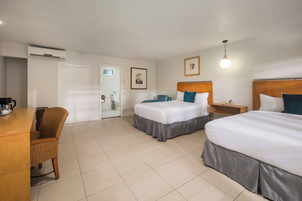 A hotel room with two beds, a desk with a coffee maker, a chair, and a wardrobe.