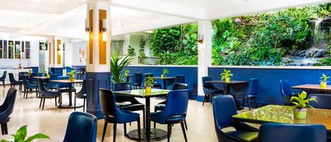 A restaurant with blue chairs and tables, a white ceiling, and a wall with a waterfall view.