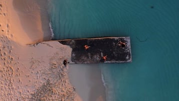 An aerial view of a beach with a wooden pier extending into the water, surrounded by footprints and a few scattered people.