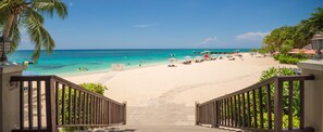 A beach with a staircase leading down to the shore, palm trees, and a clear blue sky.