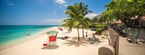 A beach with a lifeguard tower, palm trees, and a pier extending into the ocean.