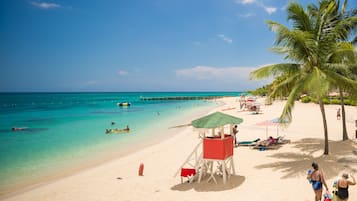 A beach with clear turquoise water, a lifeguard tower, and palm trees.