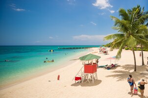 A beach with clear turquoise water, a lifeguard tower, and palm trees.