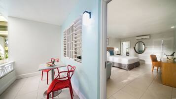 A modern hotel room with a bed, a desk, and a dining area with red chairs.