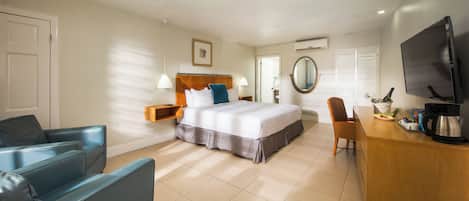 A hotel room with a bed, a desk with a coffee maker, a TV, and a chair.
