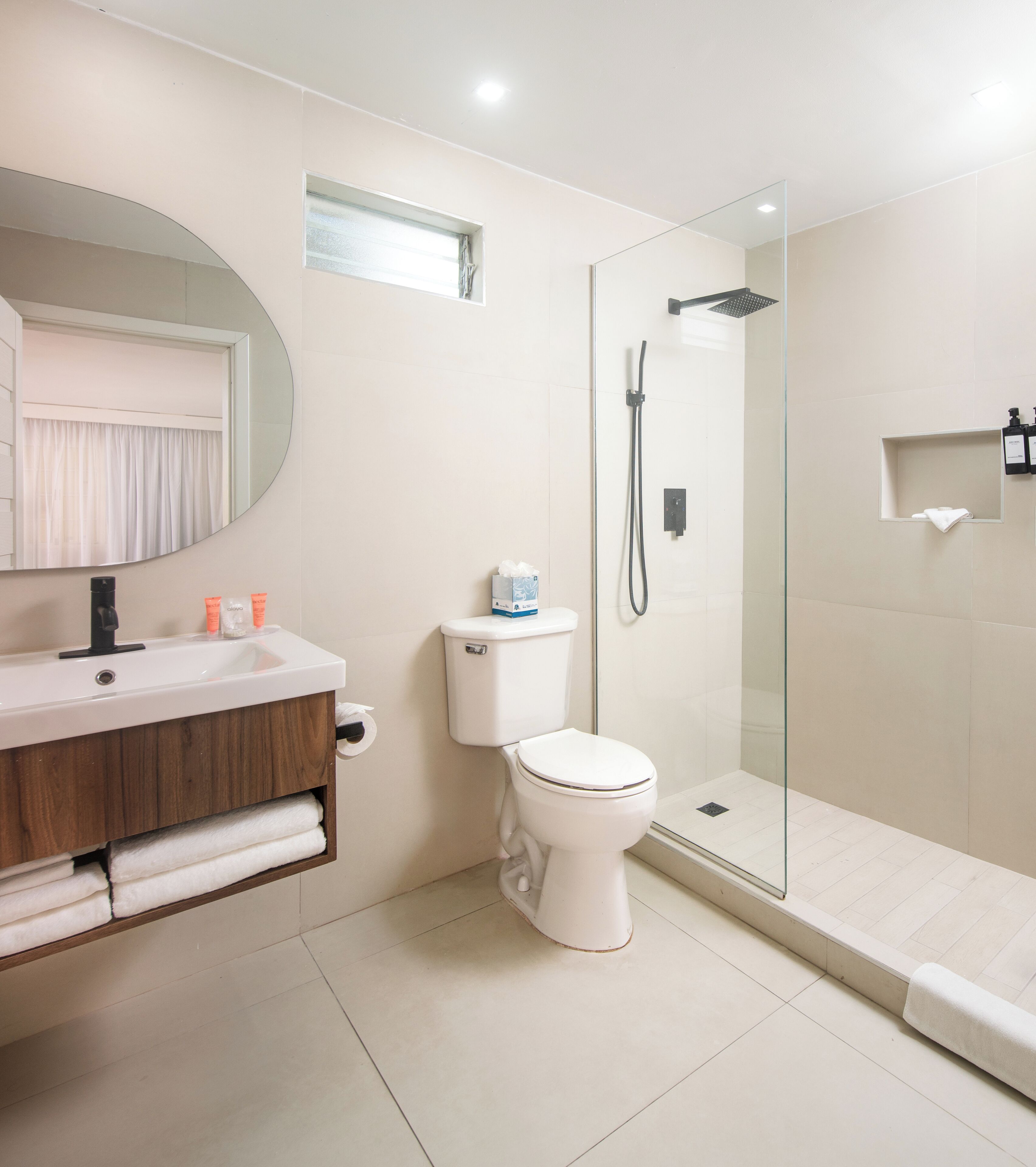 A modern bathroom with a glass-enclosed shower, a white toilet, and a vanity with a mirror and toiletries.