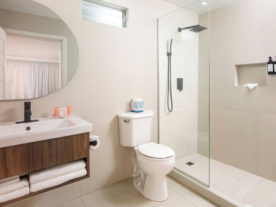 A modern bathroom with a glass-enclosed shower, a white toilet, and a vanity with a mirror and toiletries.