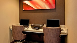 Hotelkamer met twee bureaustoelen, een bureau met twee monitoren, een printer en een groot abstract schilderij aan de muur.