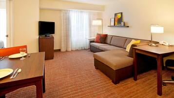 A hotel room with a dining area, a sofa, a TV, and a lamp.