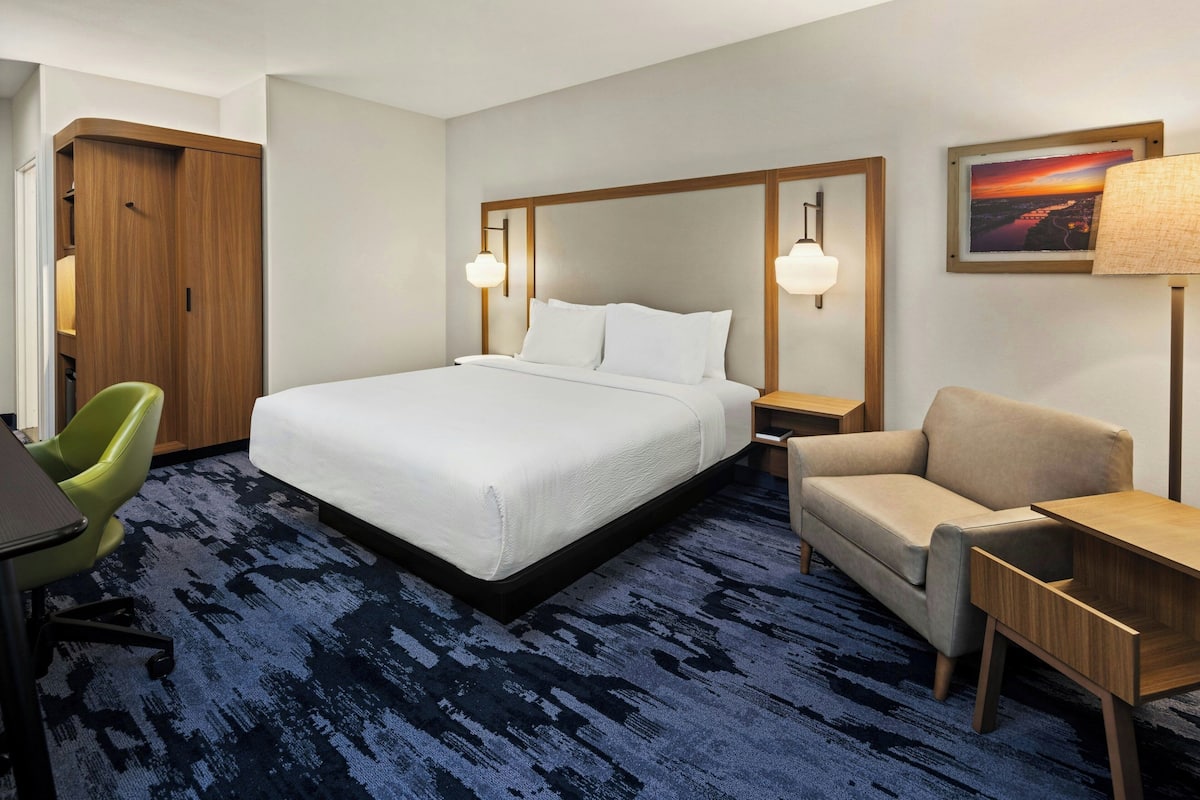 Une chambre d’hôtel avec un grand lit, un bureau, une chaise, une armoire et une table de chevet avec une lampe.