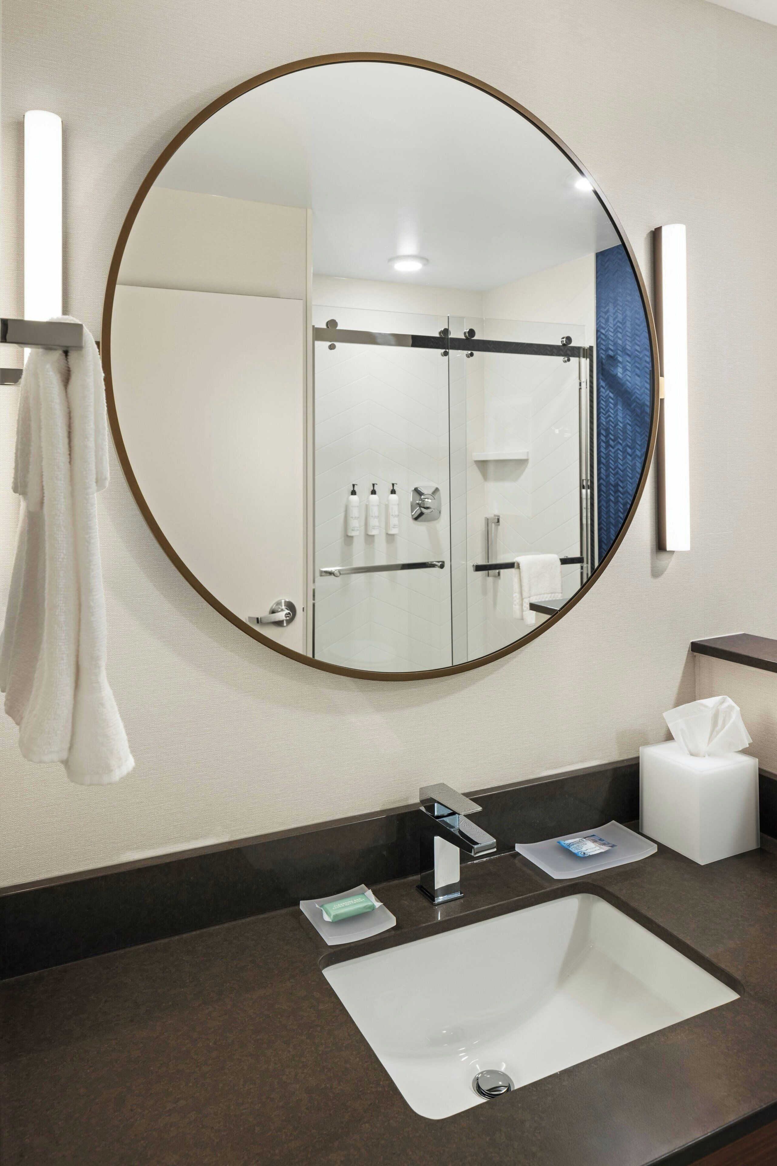 Un baño con un espejo redondo, un lavabo, toallero y zona de ducha.