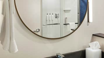 Un baño con un espejo redondo, un lavabo, toallero y zona de ducha.