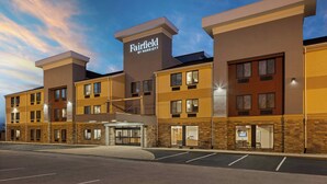 Un hotel de varios pisos con un llamativo letrero de "Fairfield by Marriott", una entrada techada y un estacionamiento.