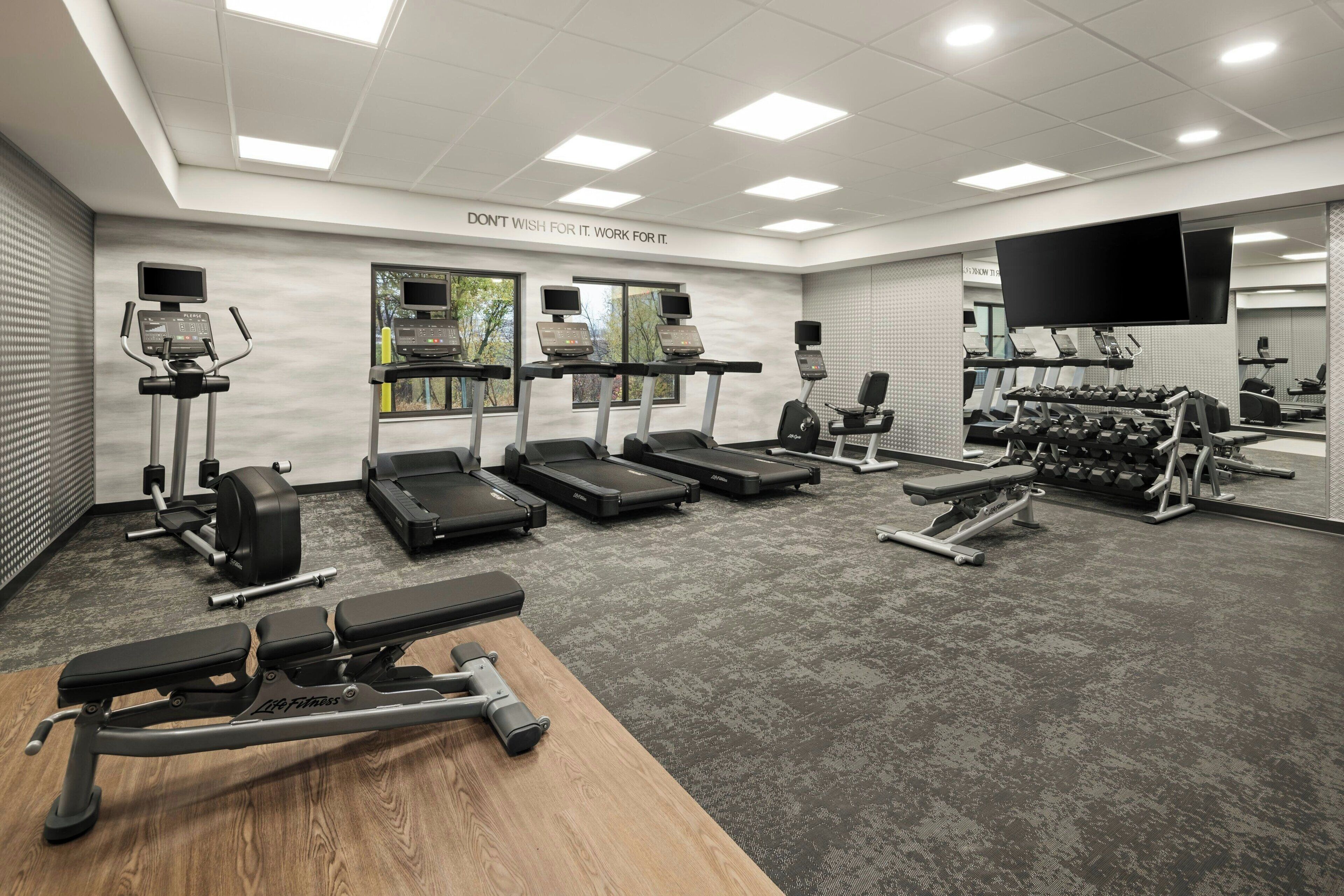 Une salle de sport moderne équipée de tapis de course, d’appareils de musculation et d’une zone dédiée au développé couché.