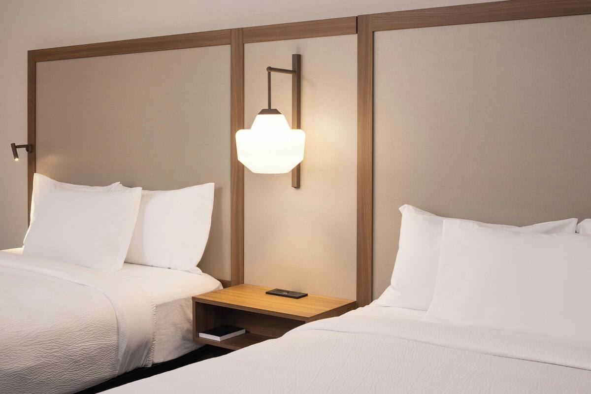 Une chambre d’hôtel avec deux lits, une table de chevet, une commode et une lampe fixée au mur.