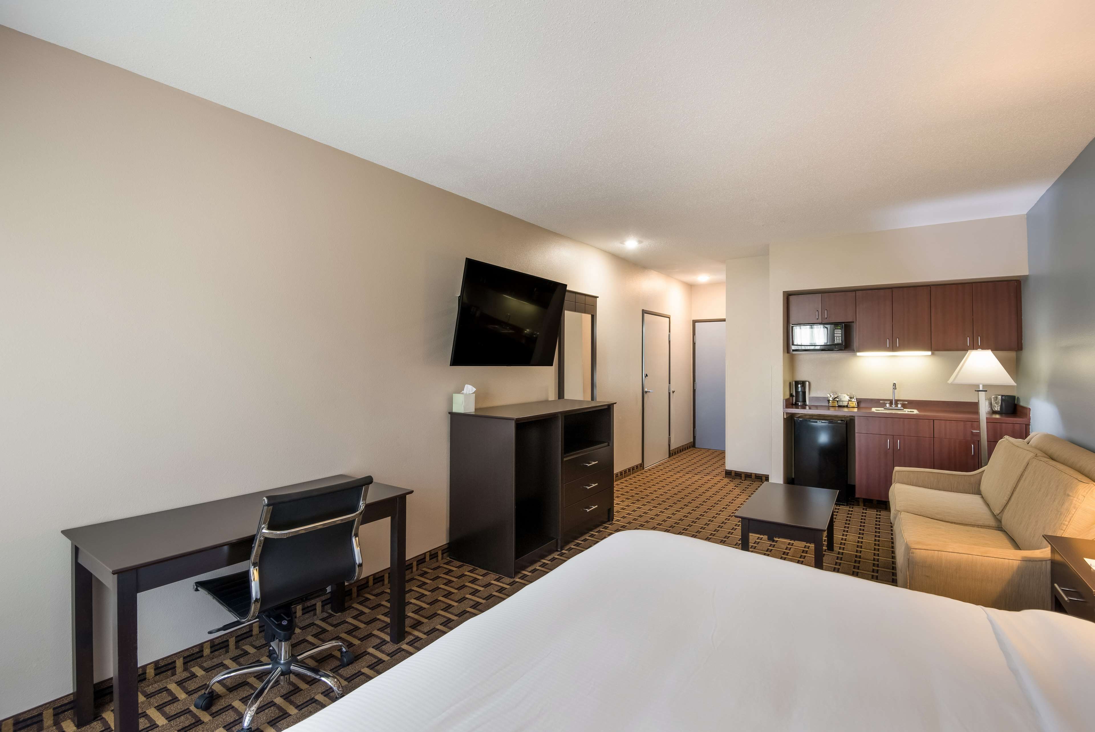 A hotel room with a bed, desk, chair, kitchenette, and TV.