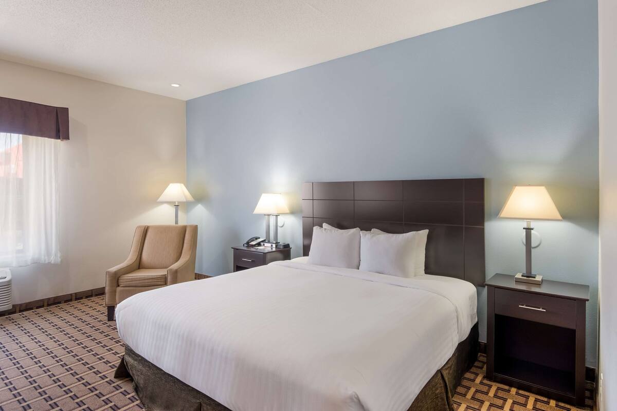 A hotel room with a large bed, two bedside tables with lamps, a chair, and a patterned carpet.