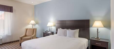 A hotel room with a large bed, two bedside tables with lamps, a chair, and a patterned carpet.