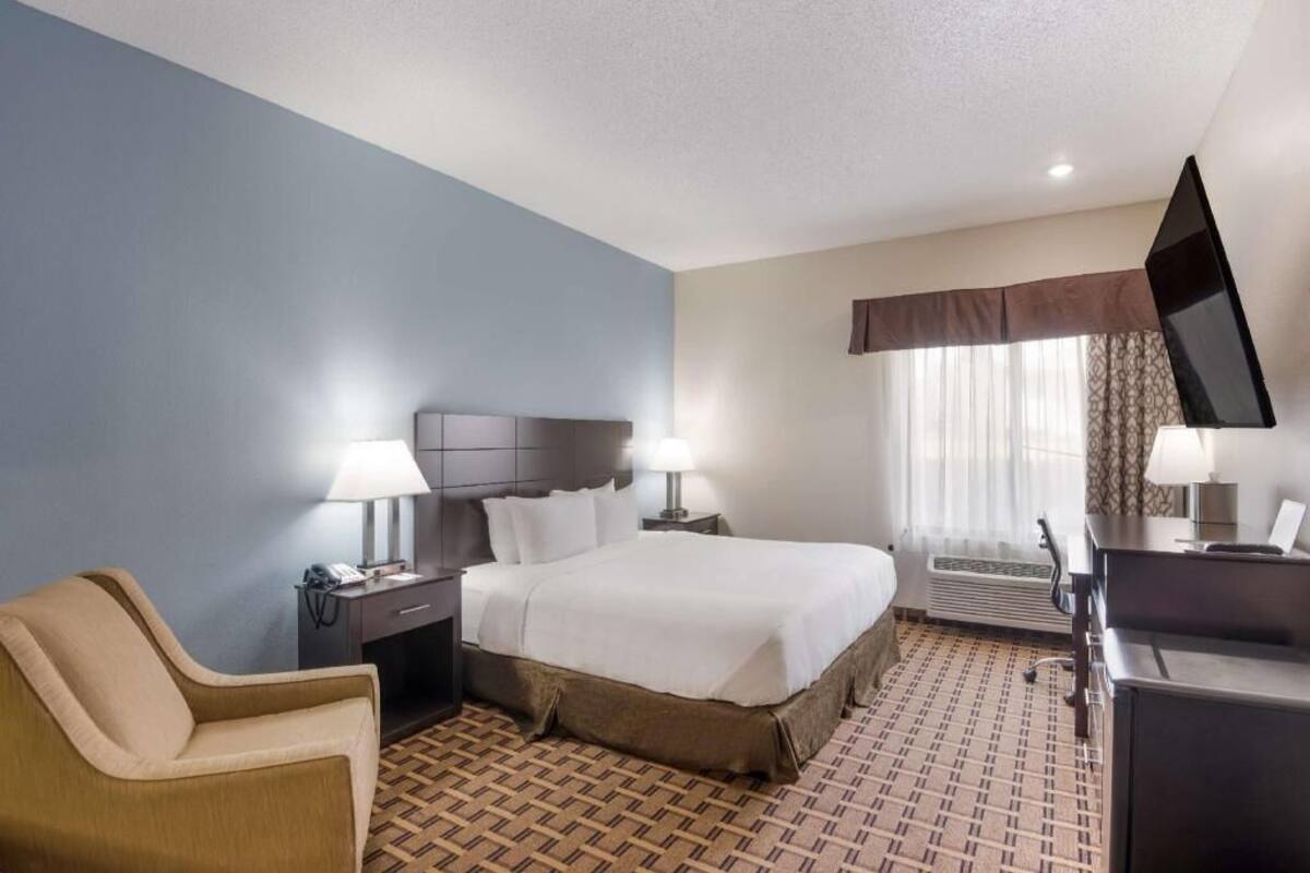 A hotel room with a bed, bedside tables, a desk, a chair, and a TV.