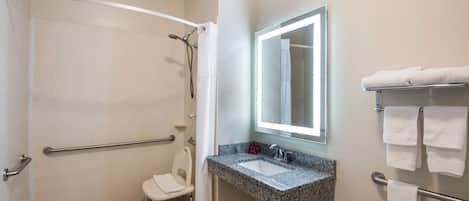 Un baño con ducha, lavamanos, espejo e inodoro.