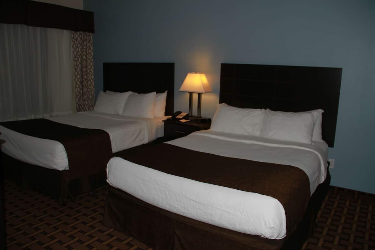 A hotel room with two beds, a nightstand with a lamp, and a patterned carpet.