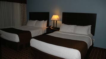 Habitación de hotel con dos camas, una mesita de noche con lámpara y alfombra estampada.