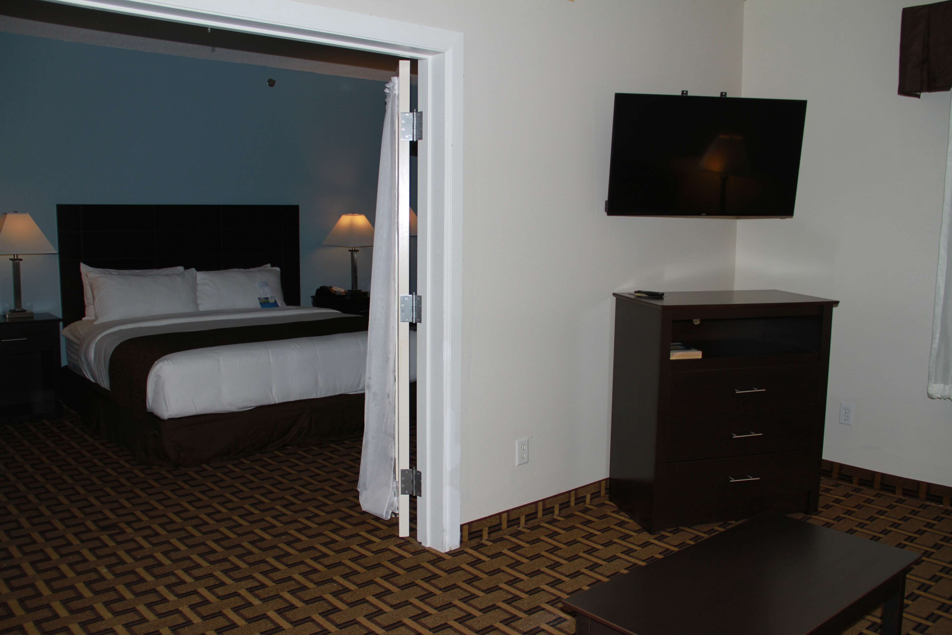 A hotel room with a bed, a TV mounted on the wall, a dresser, and a patterned carpet.