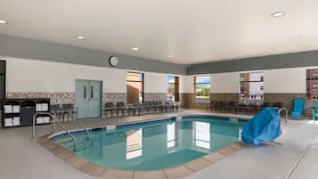 Une piscine recouverte d’une bâche bleue, une horloge au mur et un espace détente avec des chaises et des tables.