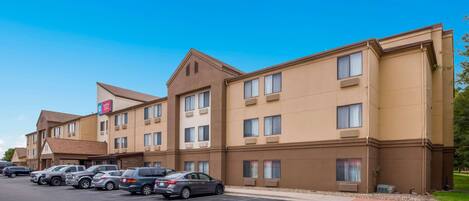 A hotel with multiple floors, a parking lot, and a clear blue sky.