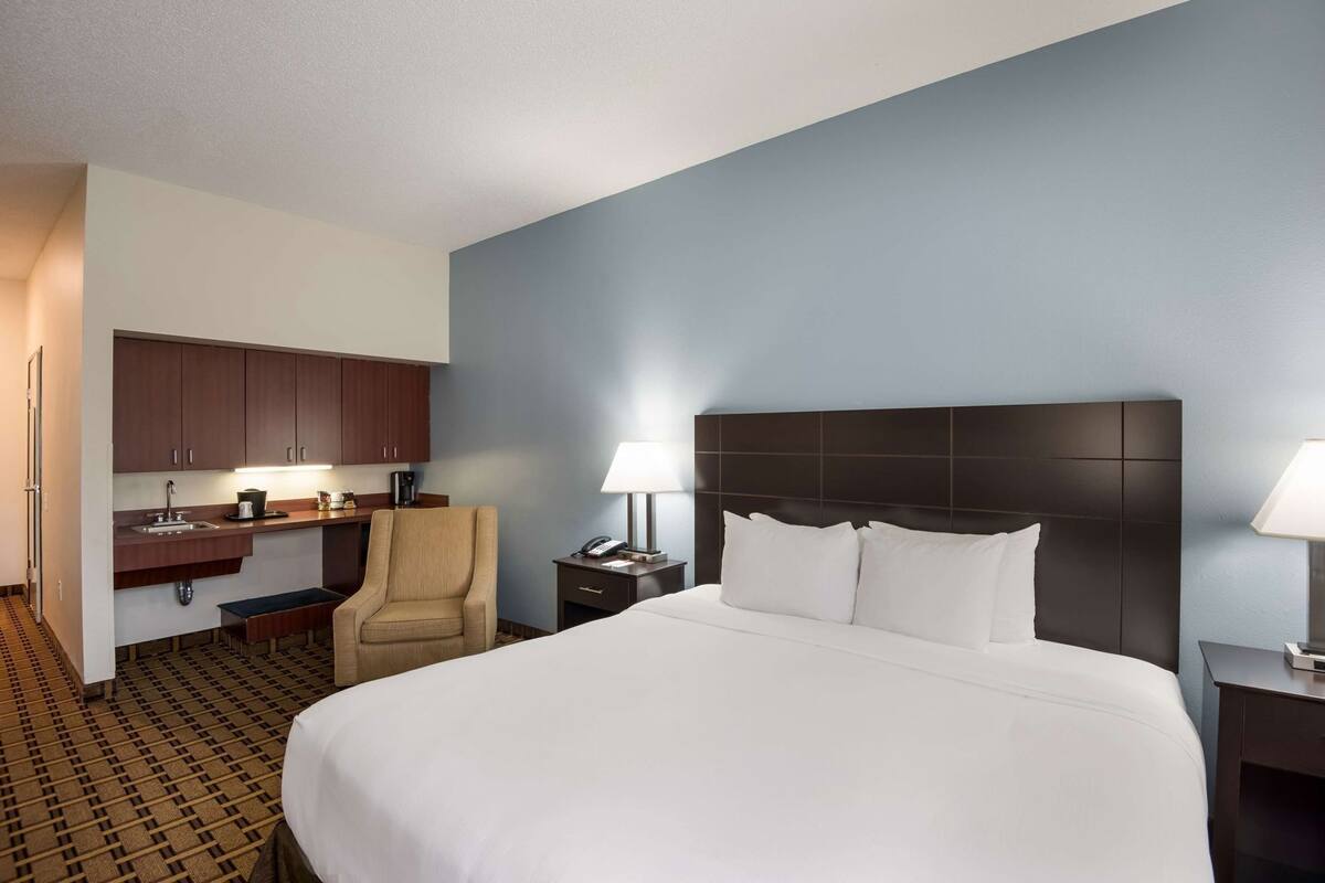 Ein Hotelzimmer mit einem Bett, einem Schreibtisch mit Stuhl, einem Nachttisch und einem an der Wand befestigten Kopfteil.