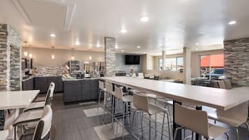 Un restaurante moderno con una barra larga, taburetes y zona de cocina.