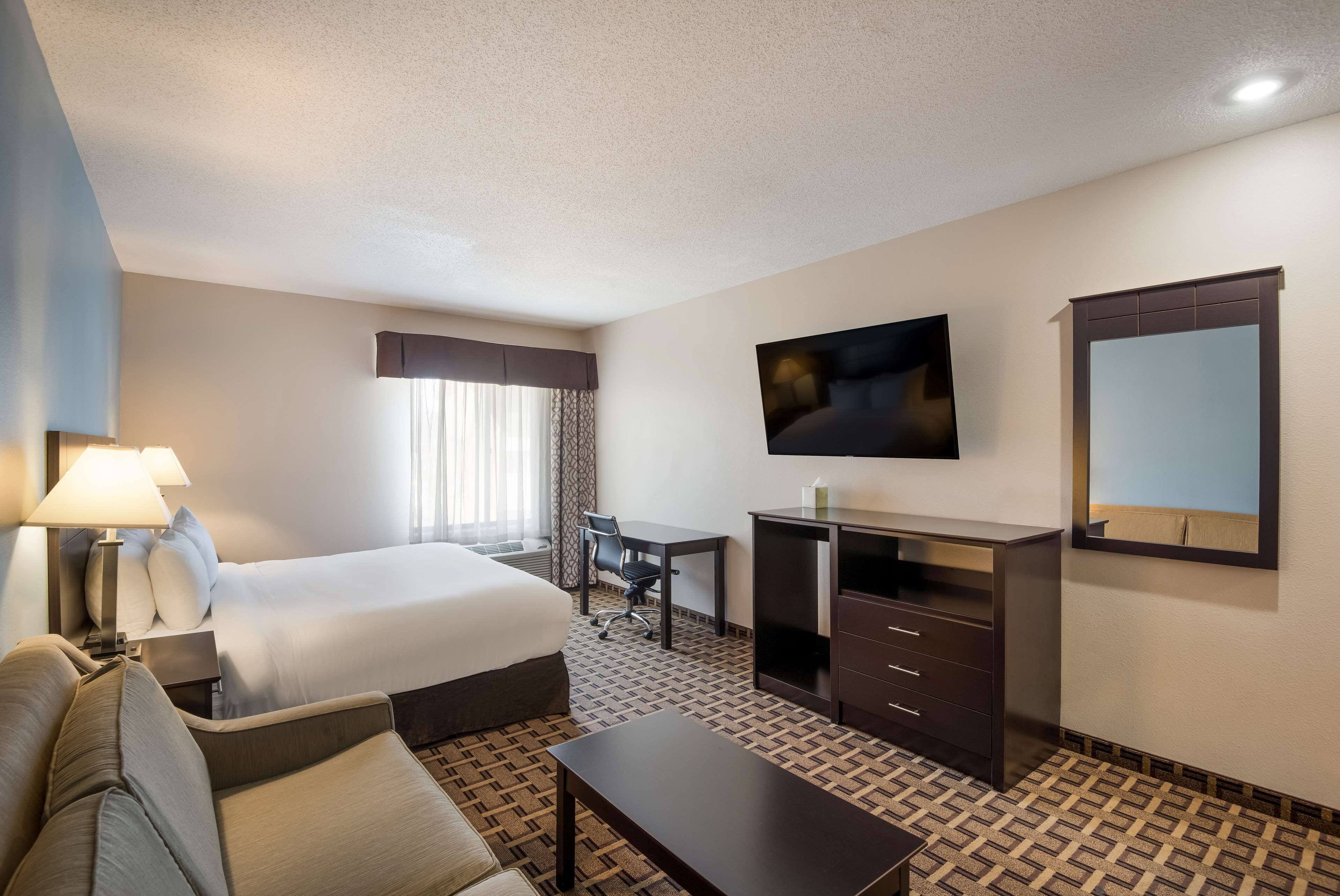 Una habitación de hotel con cama, escritorio, televisor y espejo.