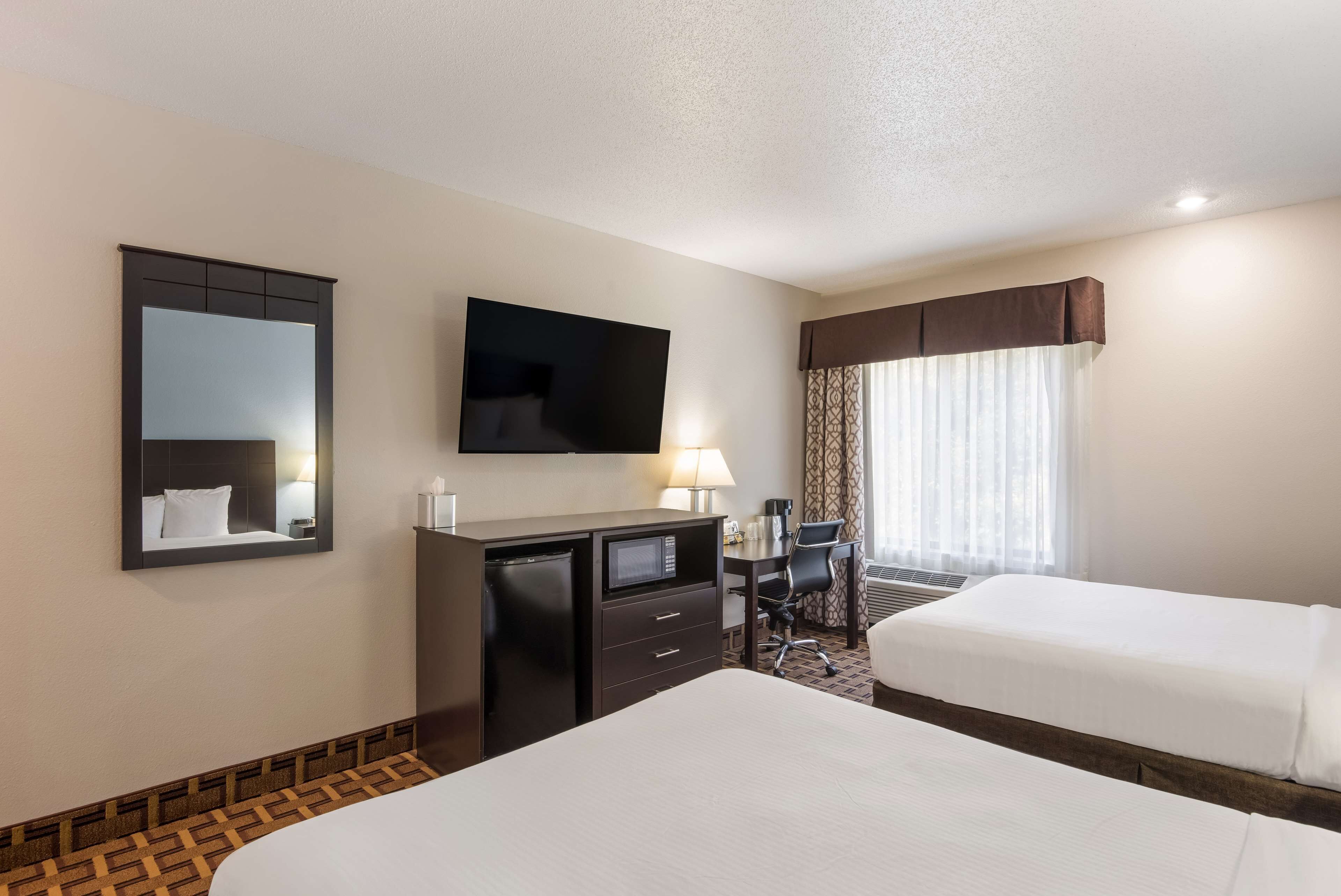 A hotel room with two beds, a desk, a television, a mirror, and a window with curtains.