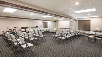 A conference room with white chairs arranged in rows, a large screen, and a drum set in the background.