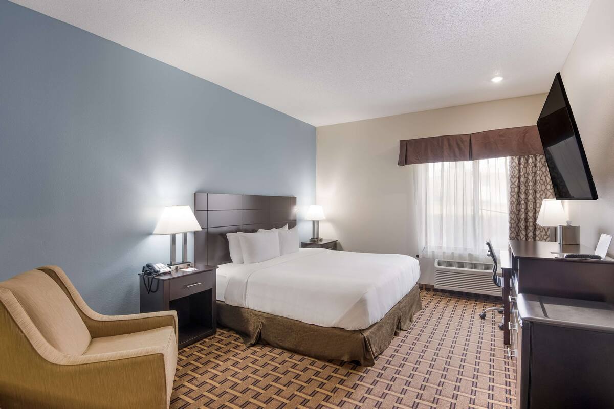 A hotel room with a bed, a chair, a desk, a TV, and a window with curtains.