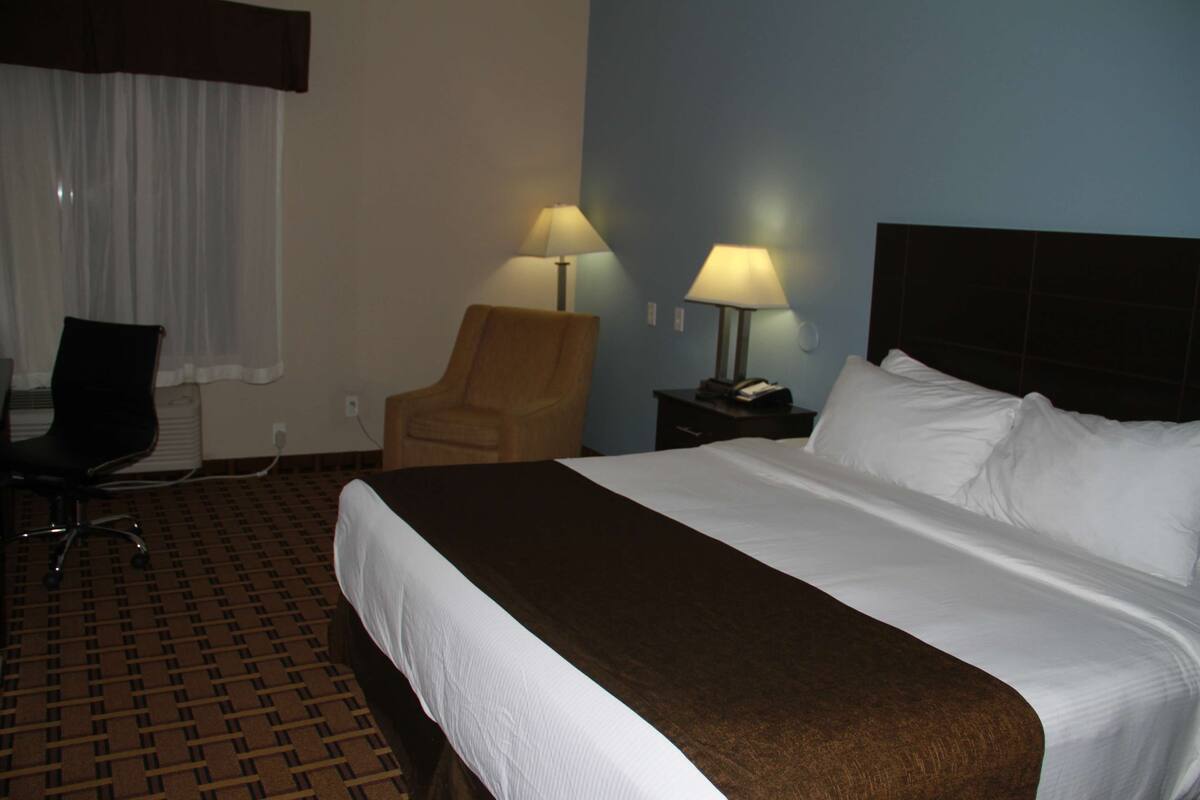 A hotel room with a large bed, two bedside lamps, a chair, and a desk.