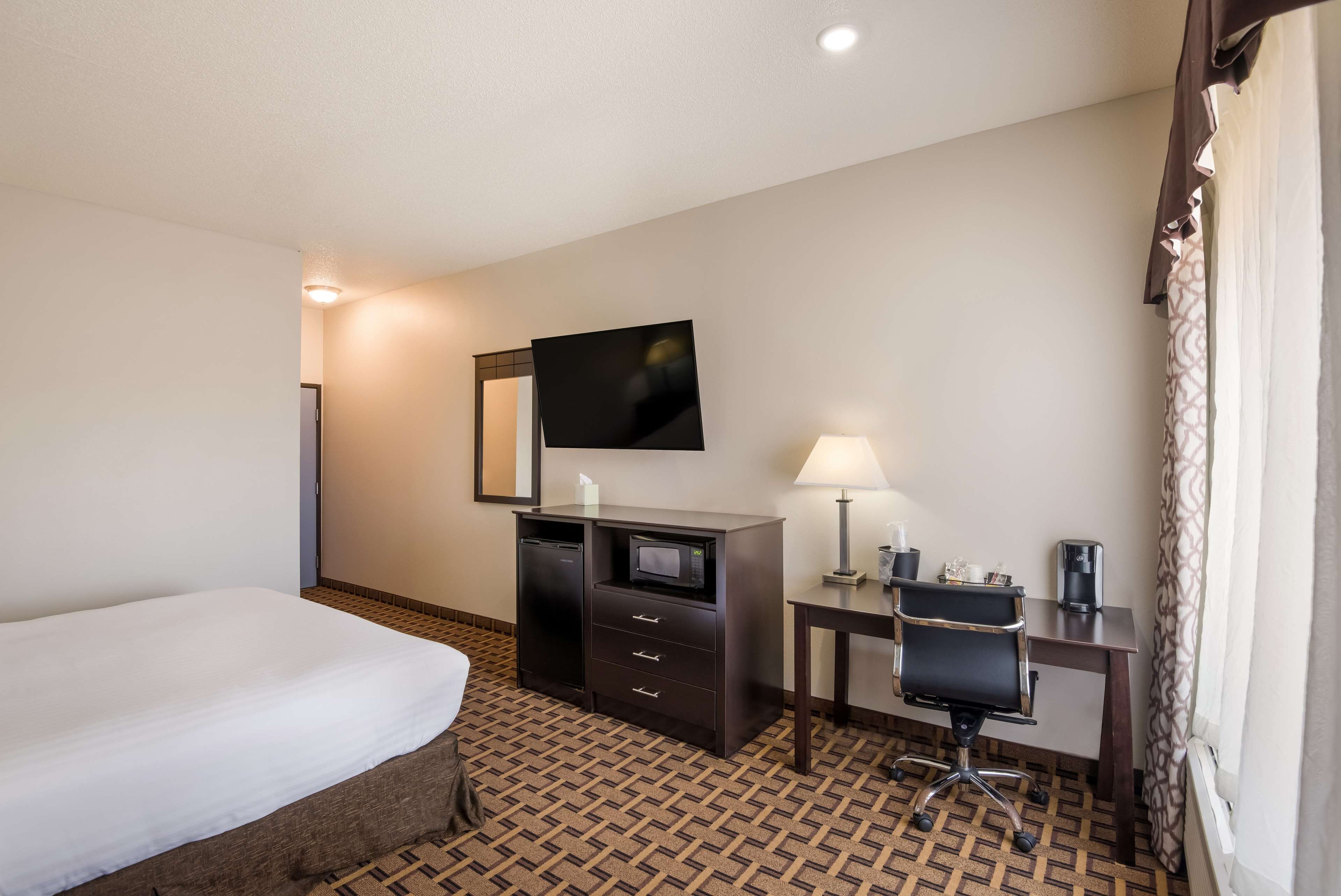 A hotel room with a bed, a desk with a chair, a television, a desk lamp, and a microwave.
