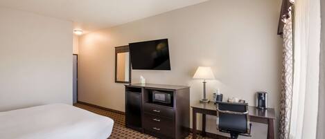 A hotel room with a bed, a desk with a chair, a television, a desk lamp, and a microwave.