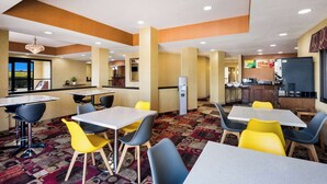 A hotel dining area with multiple tables and chairs, a kitchen area, and a view of the outdoors. - Quality Inn Des Moines North (Des Moines)