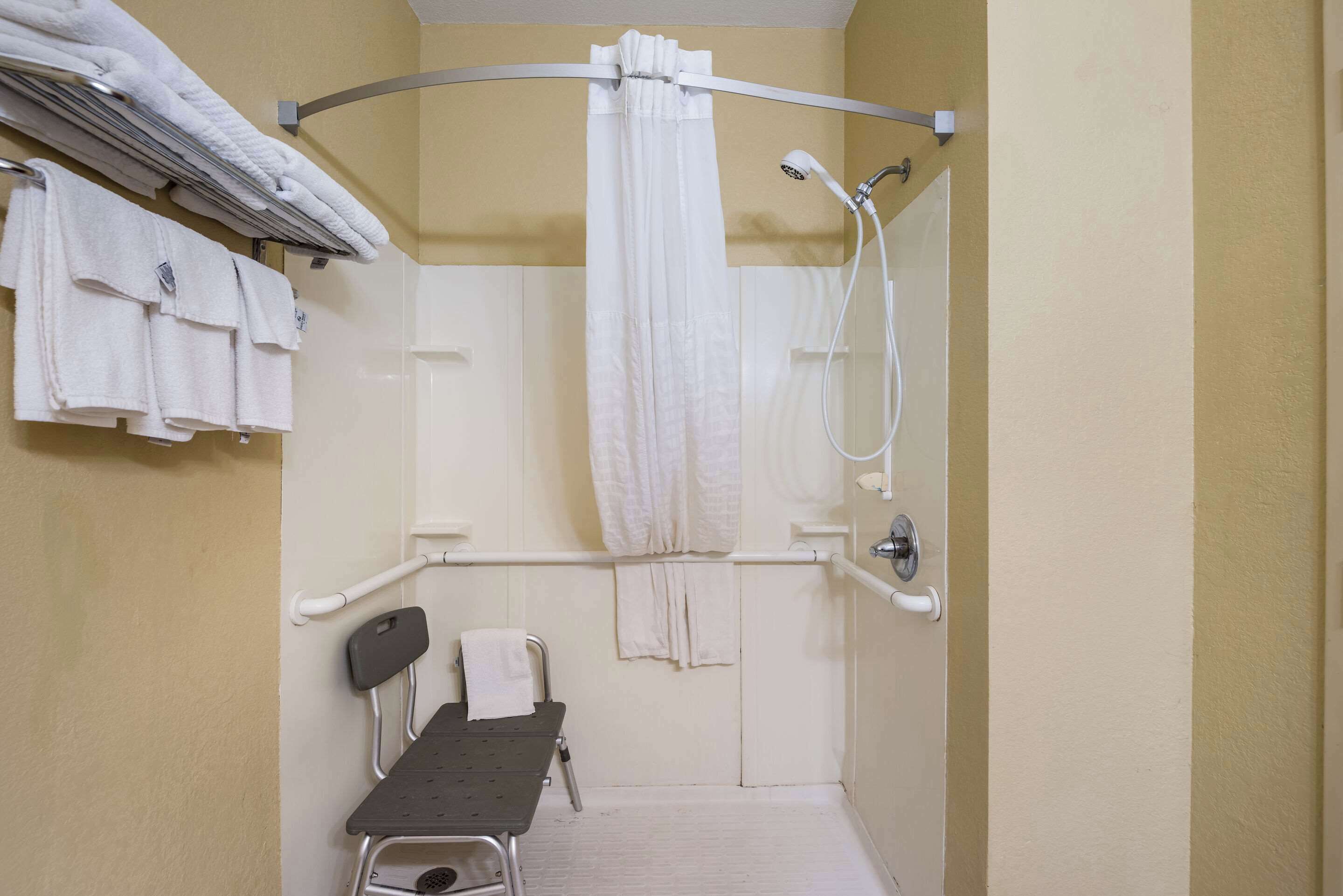 A small, private bathroom with a shower, a chair, and a towel rack.